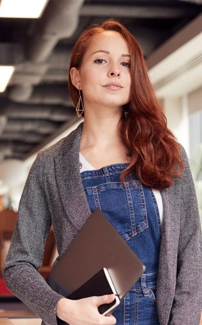 A woman with long red hair holding a laptop.